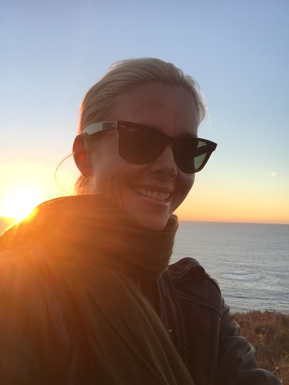 The sun setting over the ocean behind Sophie Lee, who is smiling at the camera 