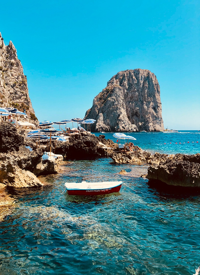 Faraglioni rocks scattered around the Capri coast, with white and blue umbrellas perched upon them for shade 