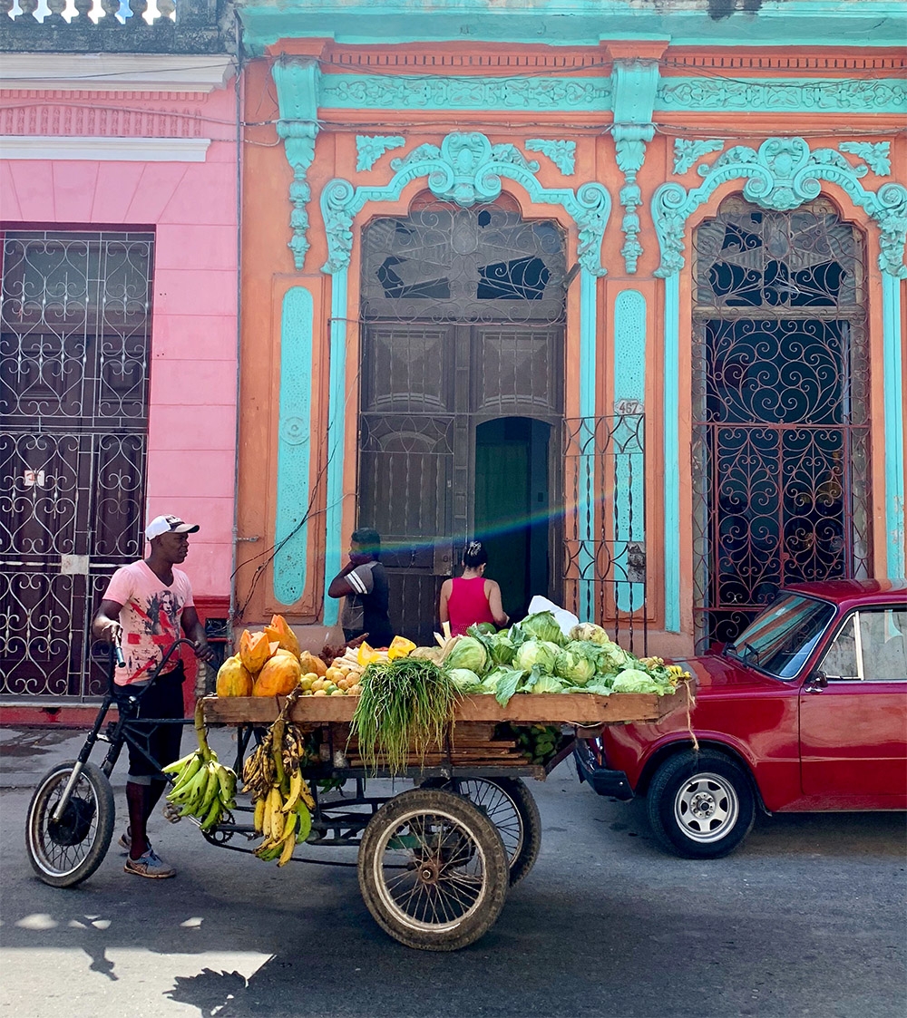 Brightly coloured buildings are on every corner, and a man sells fruit from a bike and cart 