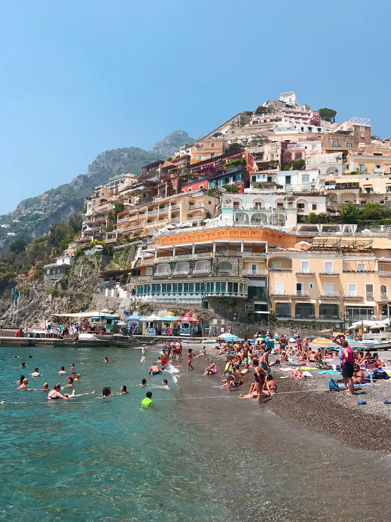 The busy main beach of Positano is surrounded by colourful buildings and a rocky shore 
