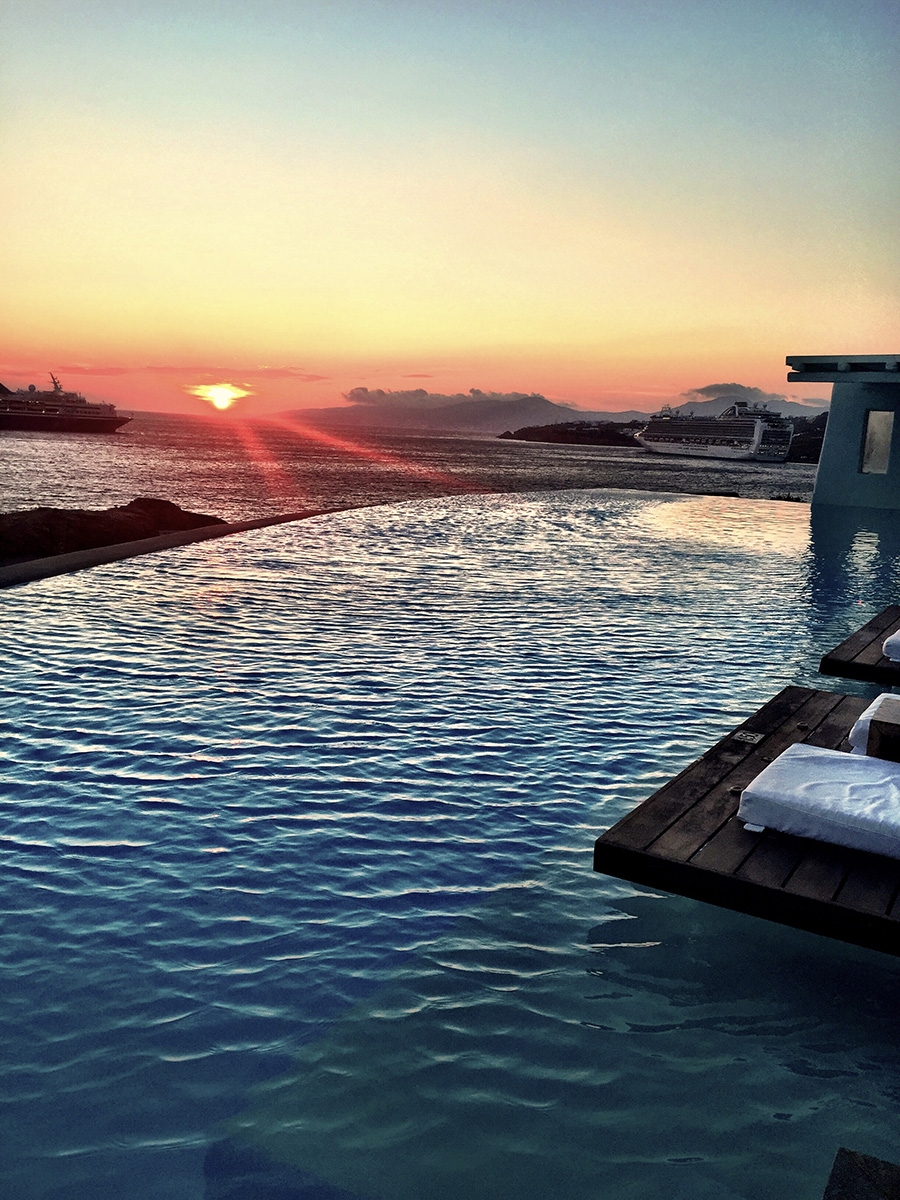 An infinity pool blends into the ocean over the horizon at sunset