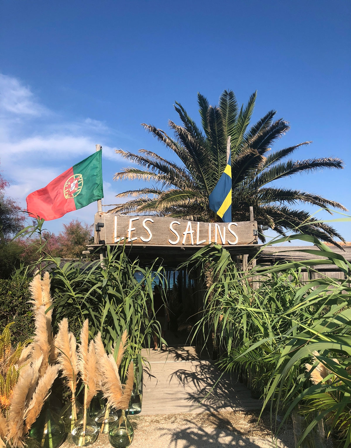 The signed entrance to Les Salins is surrounded by dense fauna and two raised flags