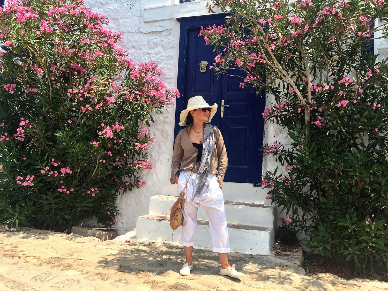 Nicky Zimmermann stands in front of a traditional white and blue Greek building, with native flowers either side of her 