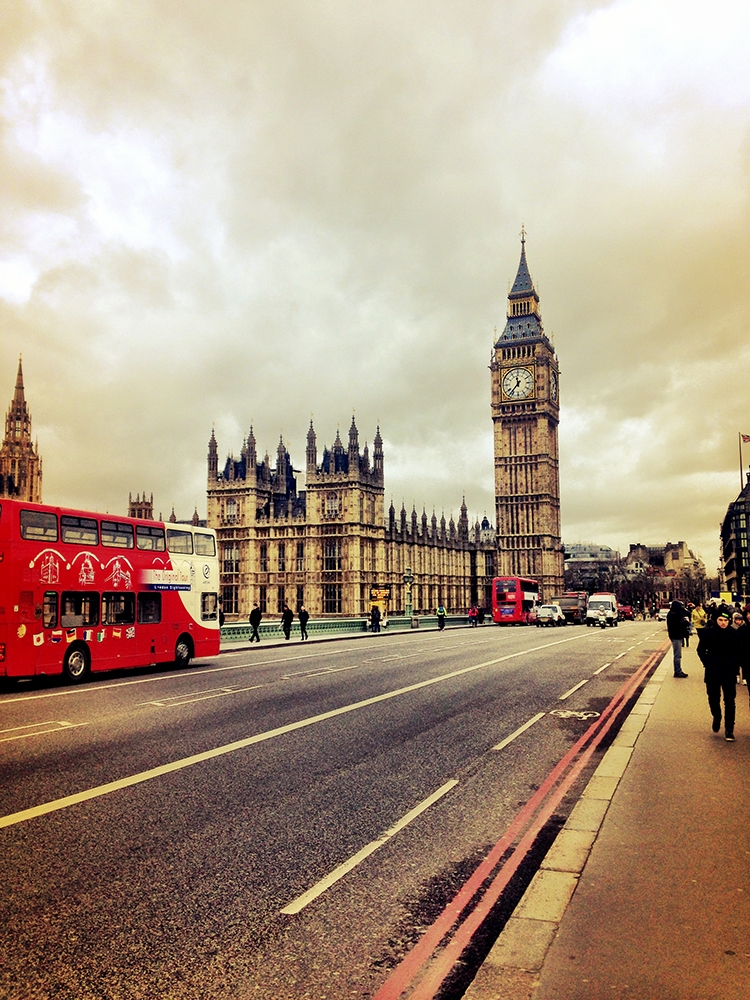 Red double decker buses drive past the Palace of Westminster and Big Ben on a cloudy day in London. February 2014 