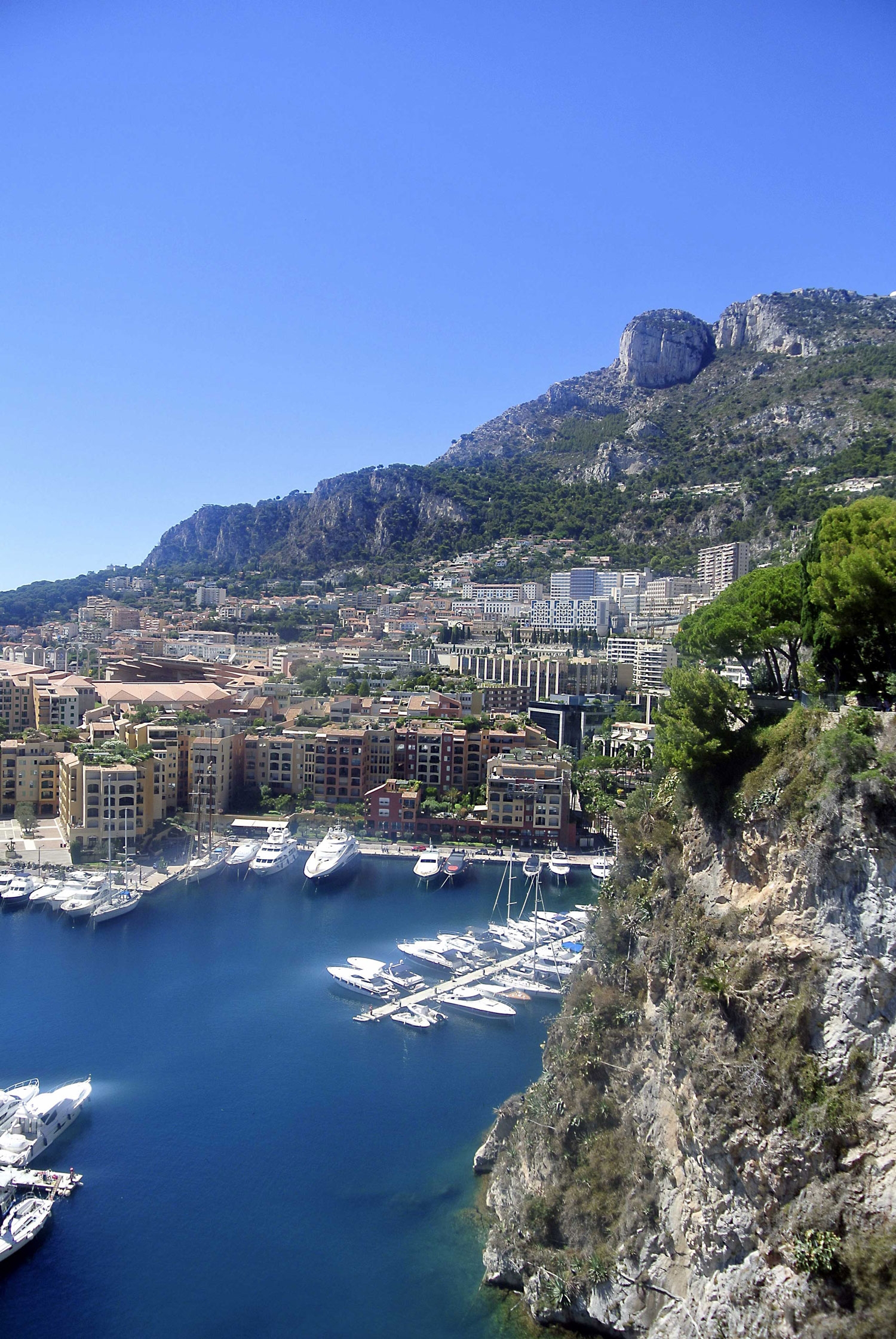 Tall buildings and large boats line the bright blue coastline of Monaco 