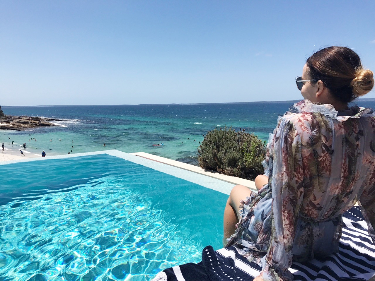 Marnie sitting by the pool, looking down at the turquoise sea below 